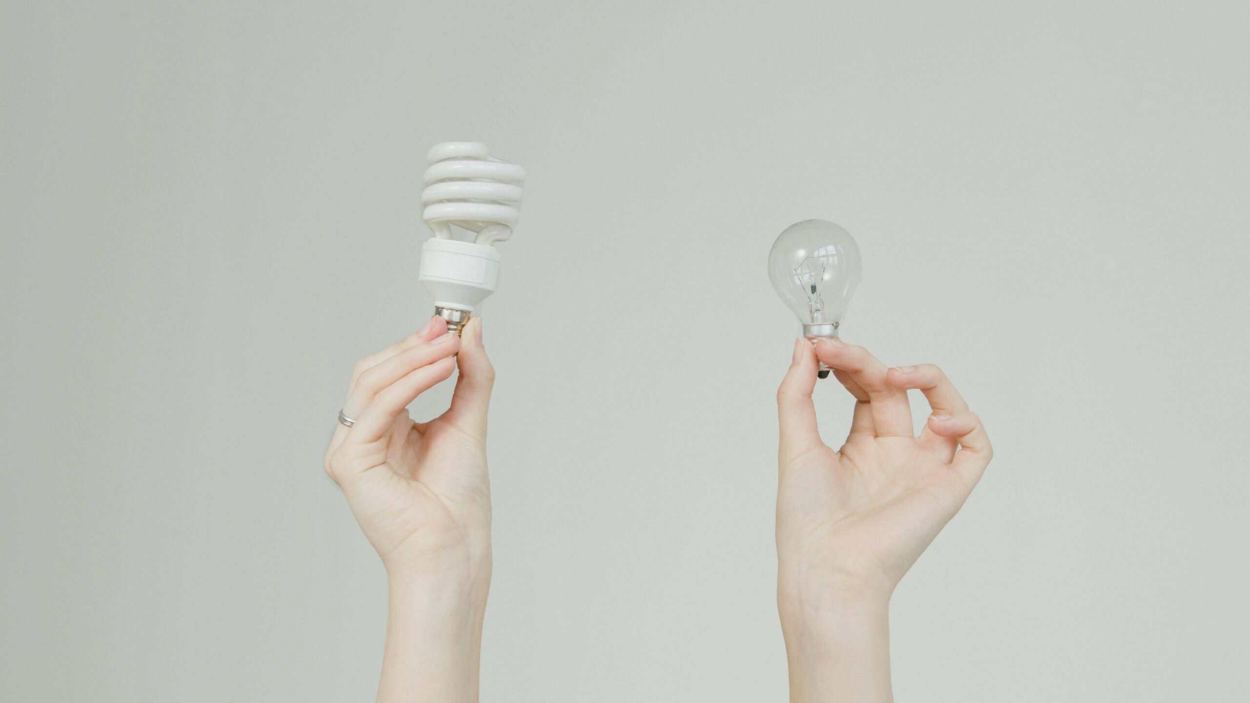 Hands hold incandescent and spiral light bulbs, symbolizing energy efficiency.